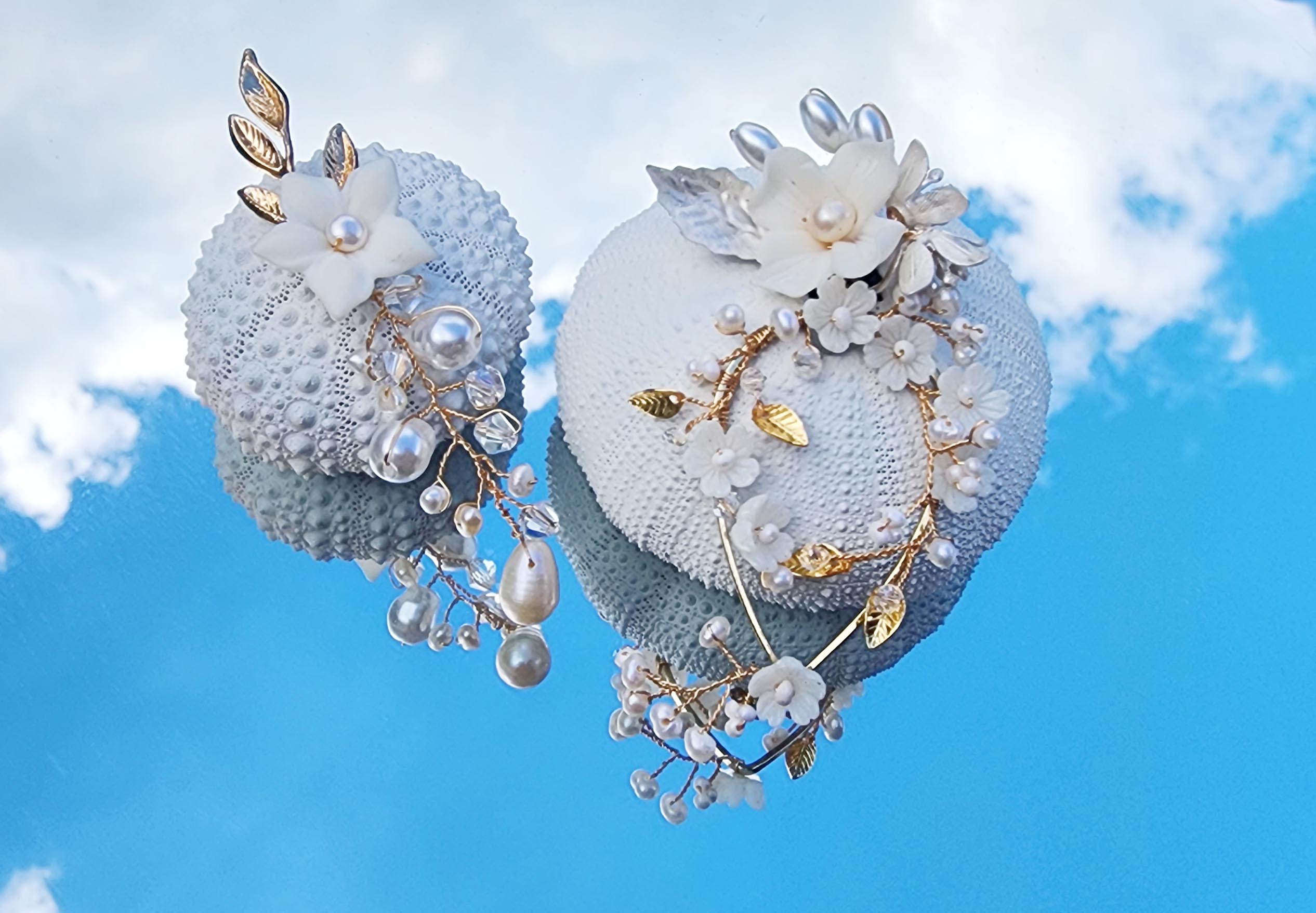 Handmade bridal earrings with freshwater pearls, porcelain flowers, and gold wire details, displayed against a blue sky background
