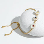 Gold adjustable bracelet with three white mother-of-pearl flower charms featuring red, blue, and clear birthstones.
