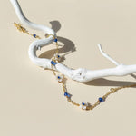 Gold necklace with blue and white beads on a white branch against a beige background