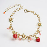 Gold bracelet with strawberry and flower charms on a white background