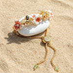 Decorative hair clip with flowers and a bee on a white stone, set against a sandy background.
