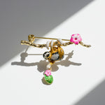Jewelry brooch with a gold branch, sloth, and pink flowers on a white background