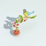 Decorative brooch with a bird, leaves, flowers, and a berry on a light blue background