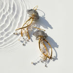 Gold and grey jellyfish-inspired earrings with pearl bead strands and resin details, displayed under ripple light.