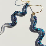 Swoosh-shaped earrings with glittery finish on a light background