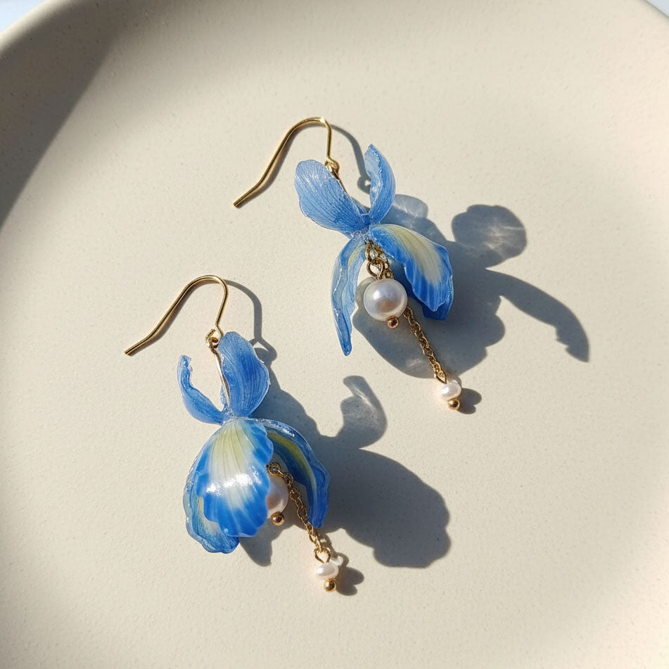 Blue flower-shaped earrings with pearl accents on a light background