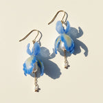 Blue iris flower drop earrings with pearls and gold chains, handcrafted resin floral jewelry on light background.