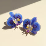 Blue orchid-shaped earrings on a beige background
