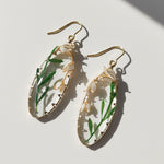Gold earrings with green leaves and white flowers on a light background