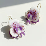Pair of floral earrings with purple and white flowers on a light background