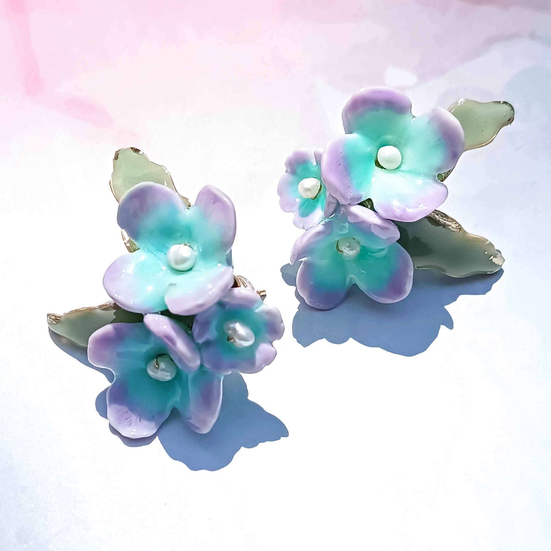 Pair of handpainted hydrangea earrings with pastel colors on a soft gradient background