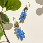 Blue floral earrings with green beads on a beige background with leaves.