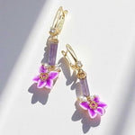 Gold earrings with purple floral charms on a light background