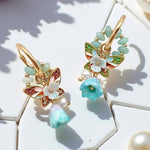Butterfly-shaped earrings with gold accents and turquoise stones on a white surface