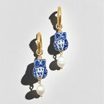Pair of earrings with blue and white floral design and gold accents on a light gray background