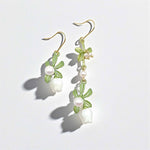 Pair of floral earrings with green leaves and white flowers on a light gray background