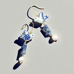 Earrings with blue and white bird designs, pearls, and blue beads on a gray background