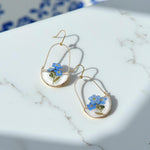 Gold earrings with blue floral elements on a marble surface