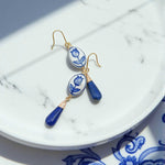 Blue and white ceramic earrings with gold accents on a marble surface
