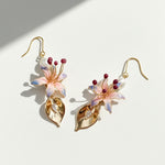 Hand-painted pink lily and gold leaf drop earrings with freshwater pearls on white background, sunlight and shadow
