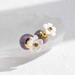 Pair of earrings with floral designs and purple beads on a white background