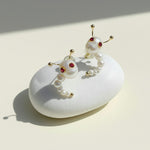 Pair of pearl earrings with red gemstones on a white stone