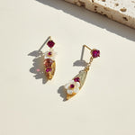 Gold earrings with red and white stones on a light surface