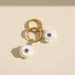 Gold earring with white floral charms and purple stones on a beige background
