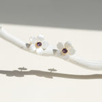 Pair of white flower earrings with purple gemstones on a white branch.
