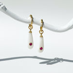 Pair of earrings with gold hooks, white teardrop-shaped stones, and red gemstones on a white background.