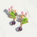 Floral-themed earrings with pink flowers, green leaves, and purple beads on a light background