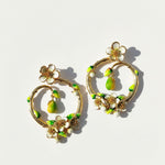Gold hoop earrings with floral and green accents on a light background