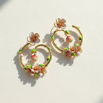 Pair of gold hoop earrings with floral and shell designs on a light background