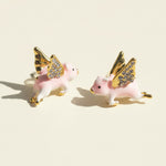 Pair of pink pig earrings with gold wings on a beige background