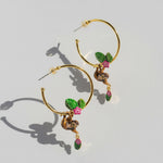 Gold hoop earrings with green leaves pink flowers and a sloth on a light gray background