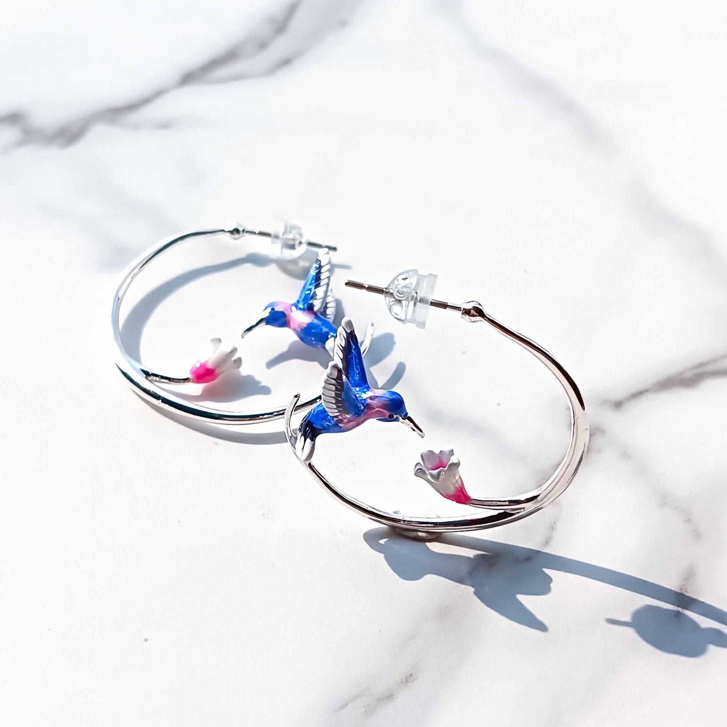 Hoop earrings with colorful hummingbird designs on a marble surface