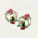 Toucan-themed earrings with floral and berry details on a white background