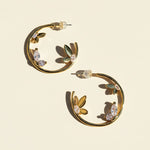 Gold hoop earrings with leaf and gemstone details on a beige background