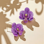 Purple flower-shaped earrings on a beige background