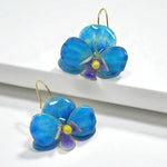Blue flower-shaped earrings with gold accents on a white surface