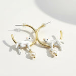 Gold hoop earrings with white cat figures on a light background