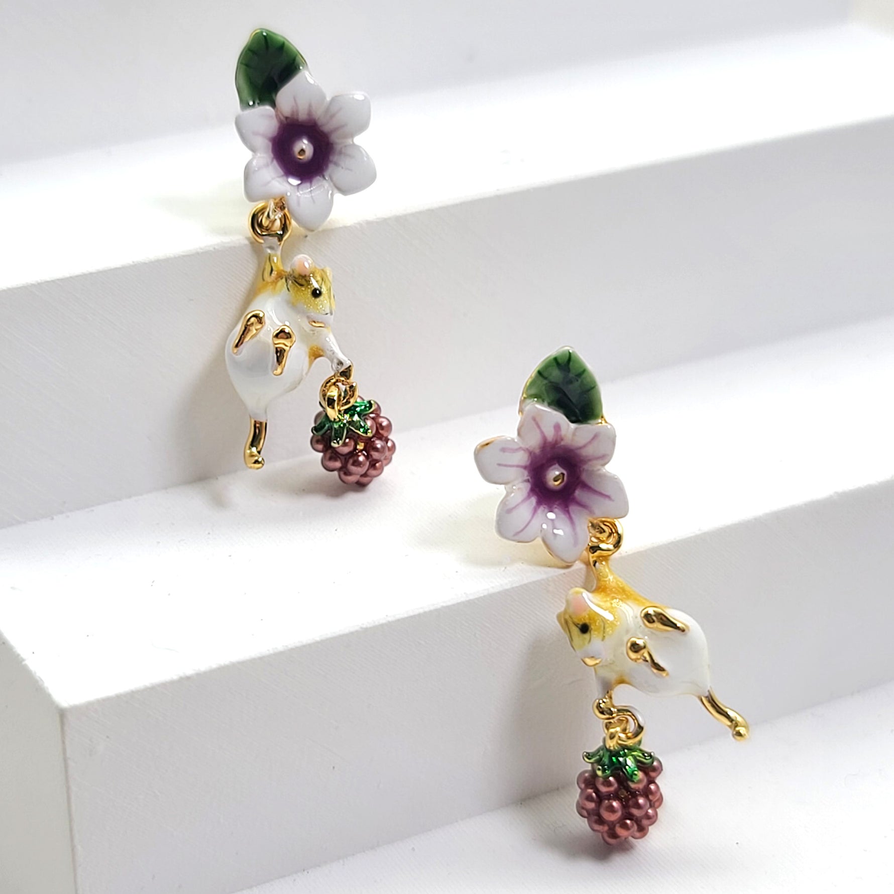 A pair of earrings featuring a gold-colored mouse and blackberry design with white and purple enamel accents.
