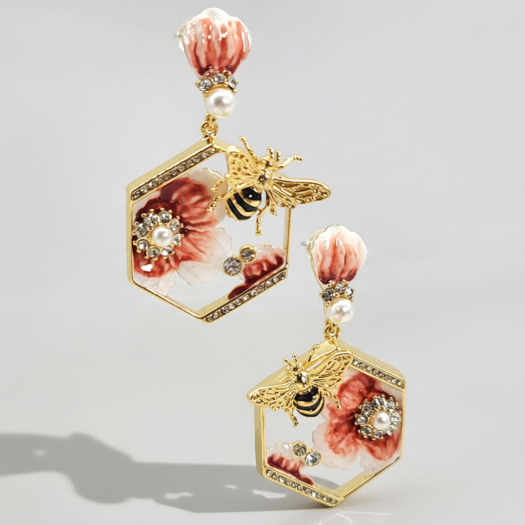 Pair of earrings with floral and bee design on a light gray background