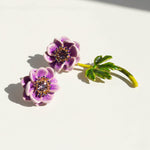 Purple flower-shaped earrings with green leaves on a white background