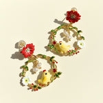 Decorative earrings with floral and chick designs on a beige background