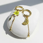 Gold hoop earrings with floral and fruit charm on a white stone surface
