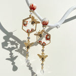 Delicate gold earrings with bee and floral designs on a white background