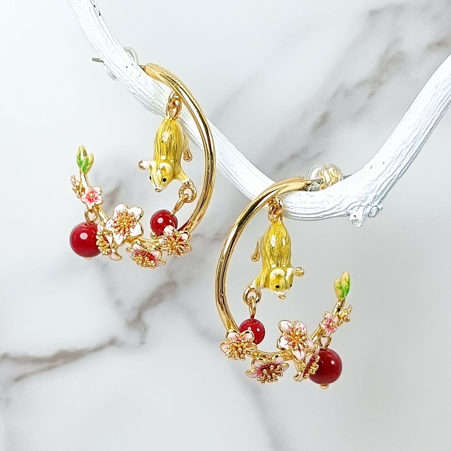 Gold-plated hoop earrings featuring hand-painted mouse charms and red floral enamel accents, displayed on a marble background.