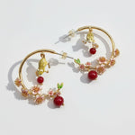 Gold hoop earrings with floral and berry designs on a light background