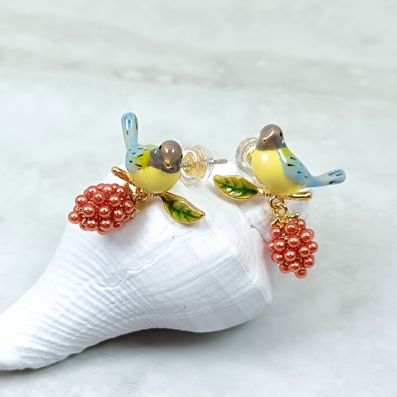 Handpainted enamel bird and berry earrings displayed on a seashell background